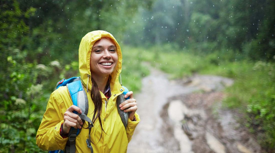 Hiker holding onto her backpack straps wearing a rain jacket and standing in the rain on a forest trail.