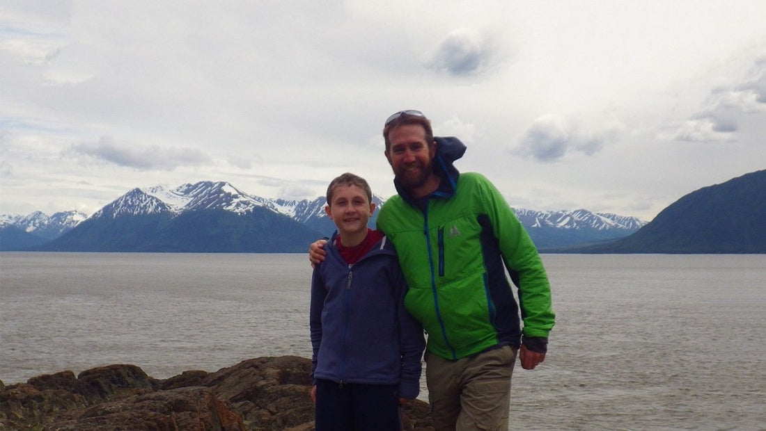 Father and son posing for a photo with the ocean and mountains in the background.