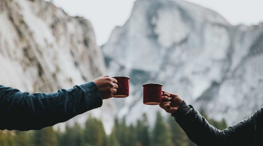 Couple raising their camp mugs of coffee with mountains in the background.