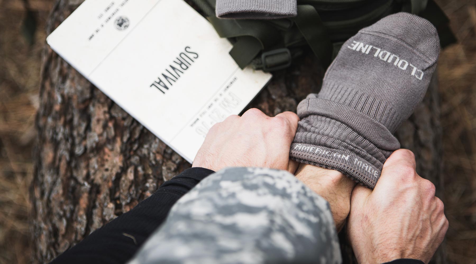 Person sitting on large log while putting on Cloudline tactical socks