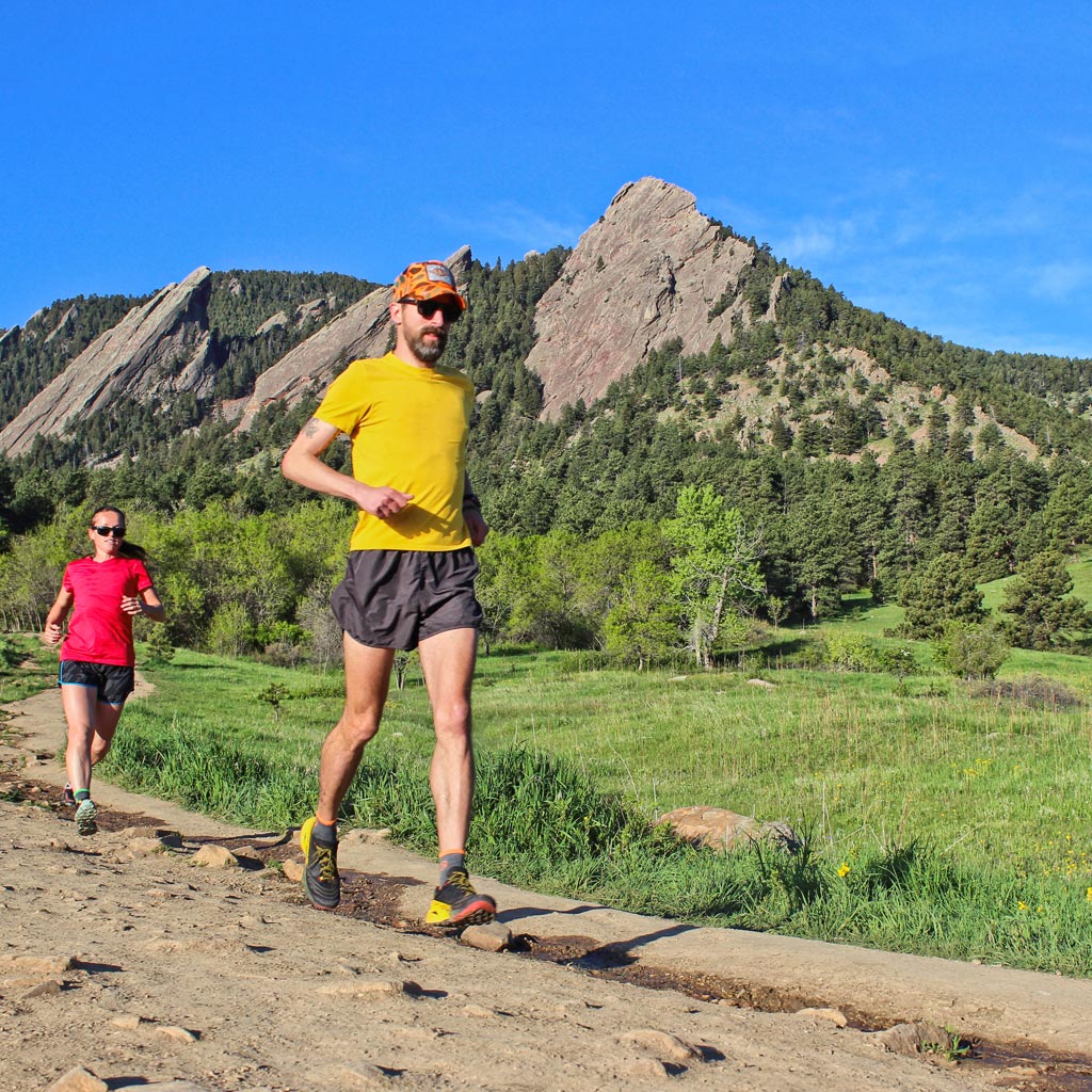 2 Trail runners running down trail with mountain towering in the distance. 