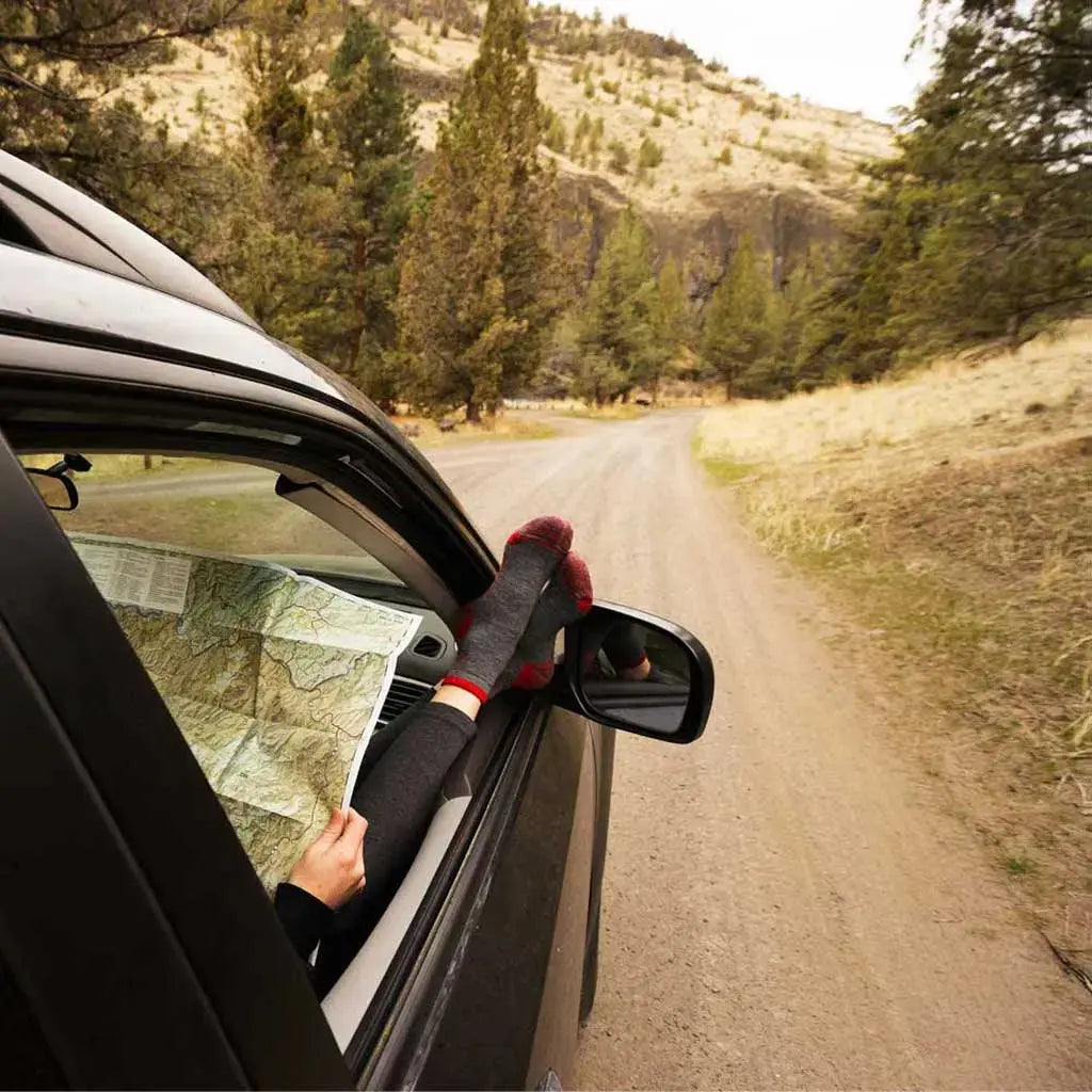 Women wearing Cloudline merino wool socks, sitting in car with feet out window checking trail map on the way to trailhead.
