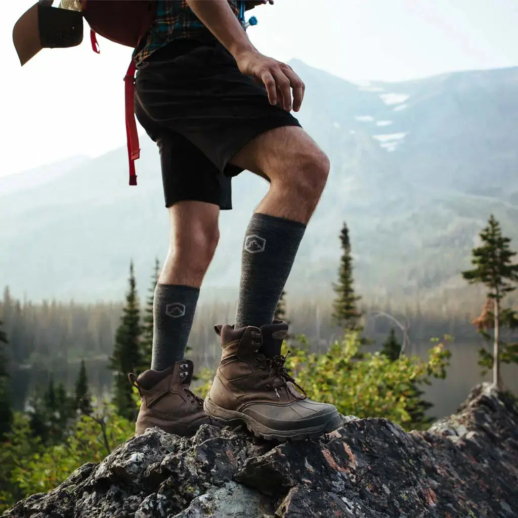 Man standing on rock above mountain lake wearing Cloudline merino wool compression socks.