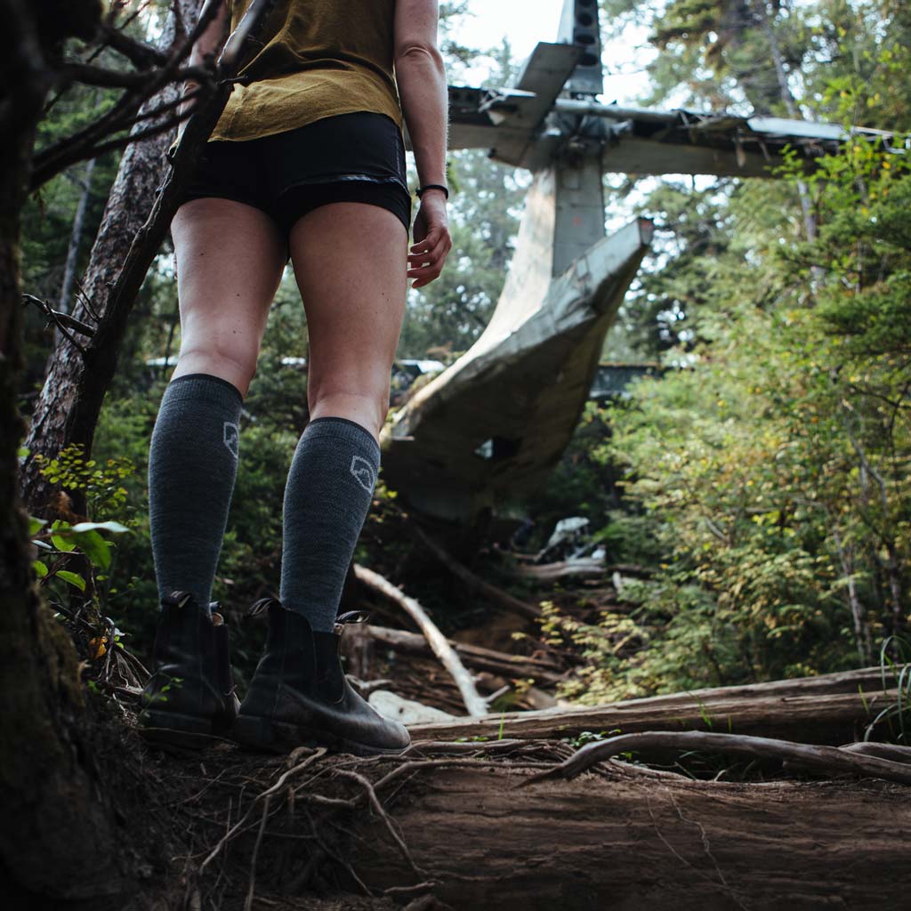 Hiker wearing Cloudline compression socks standing on log looking at plane wreckage on Vancouver Island.