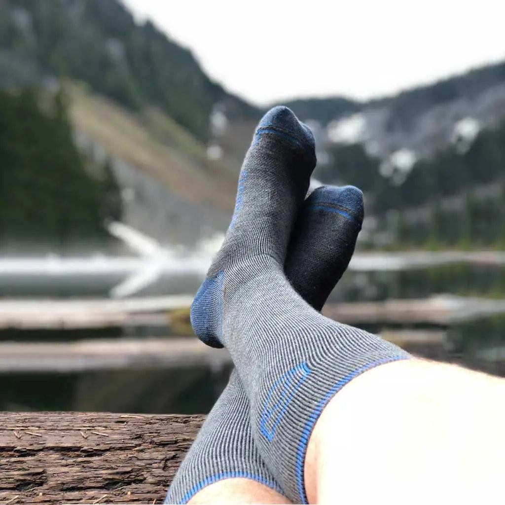 Hiker waring Cloudline merino wool compression socks laying with feet on log with mountain lake in background.
