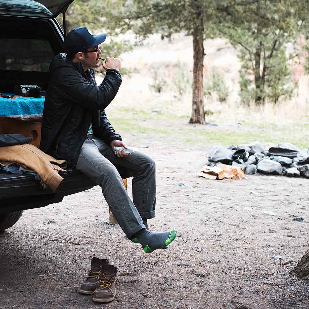 Man wearing Cloudline merino wool hiking socks, sitting on back of camper brushing teeth.