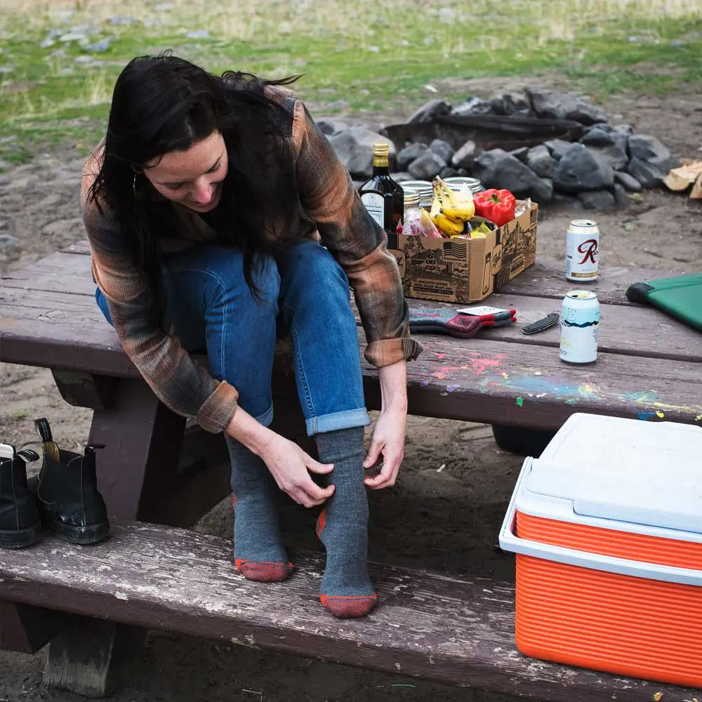 Women sitting on camp table putting on Cloudline merino wool hiking socks.