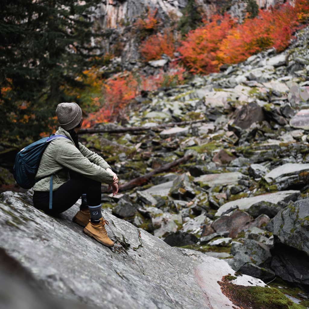 Hiker wearing Cloudline hiking socks sitting on a huge rock looking up at fall leaves.