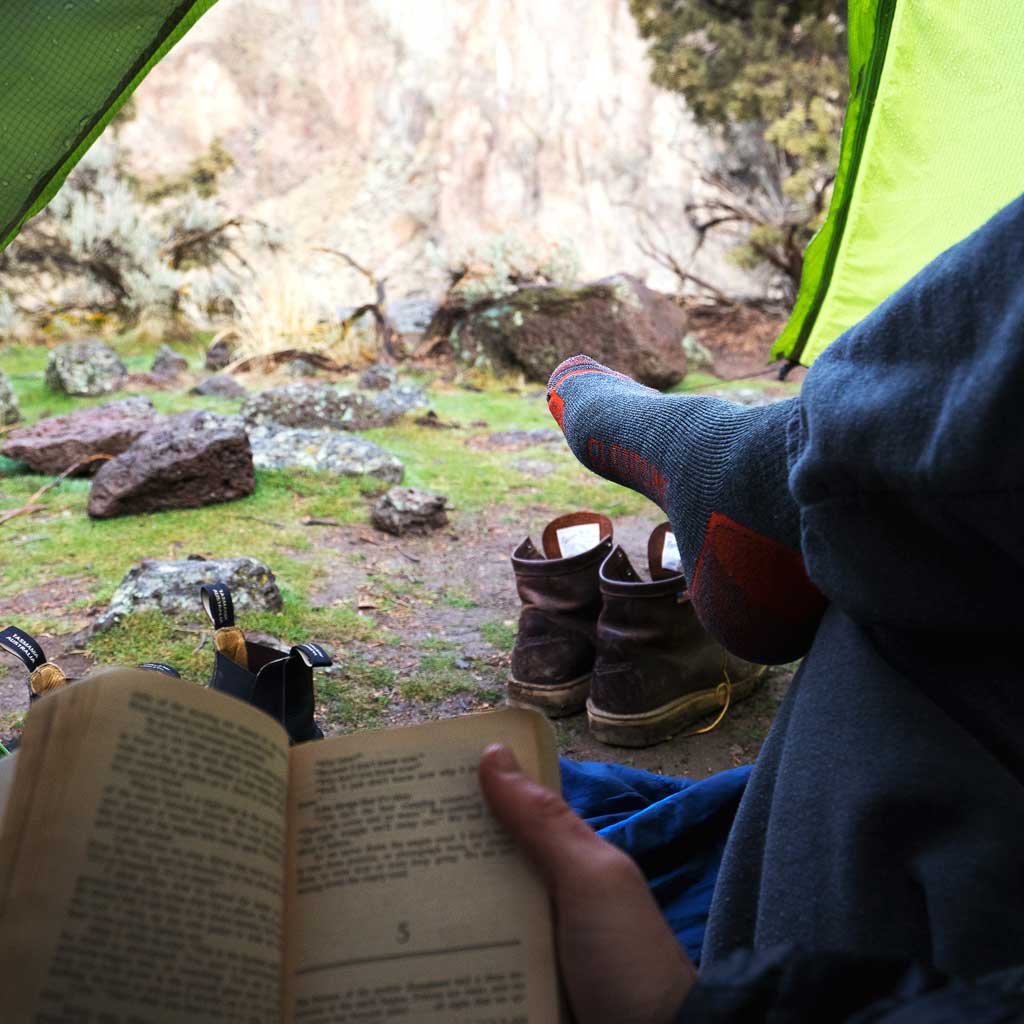 Hiker wearing Cloudline hiking socks while reading in tent.