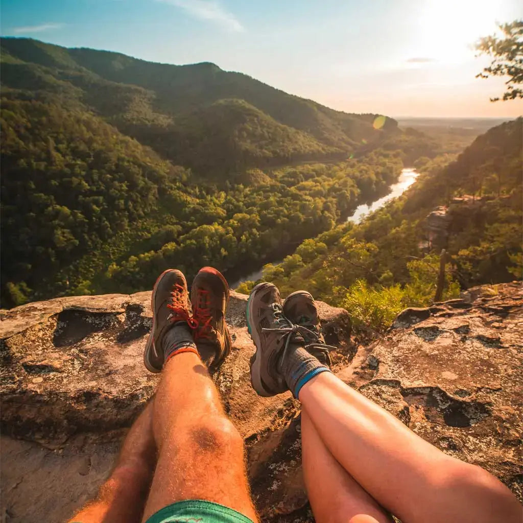 Two hikers wearing Cloudline merino wool hiking socks sitting on ridge overlooking river valley