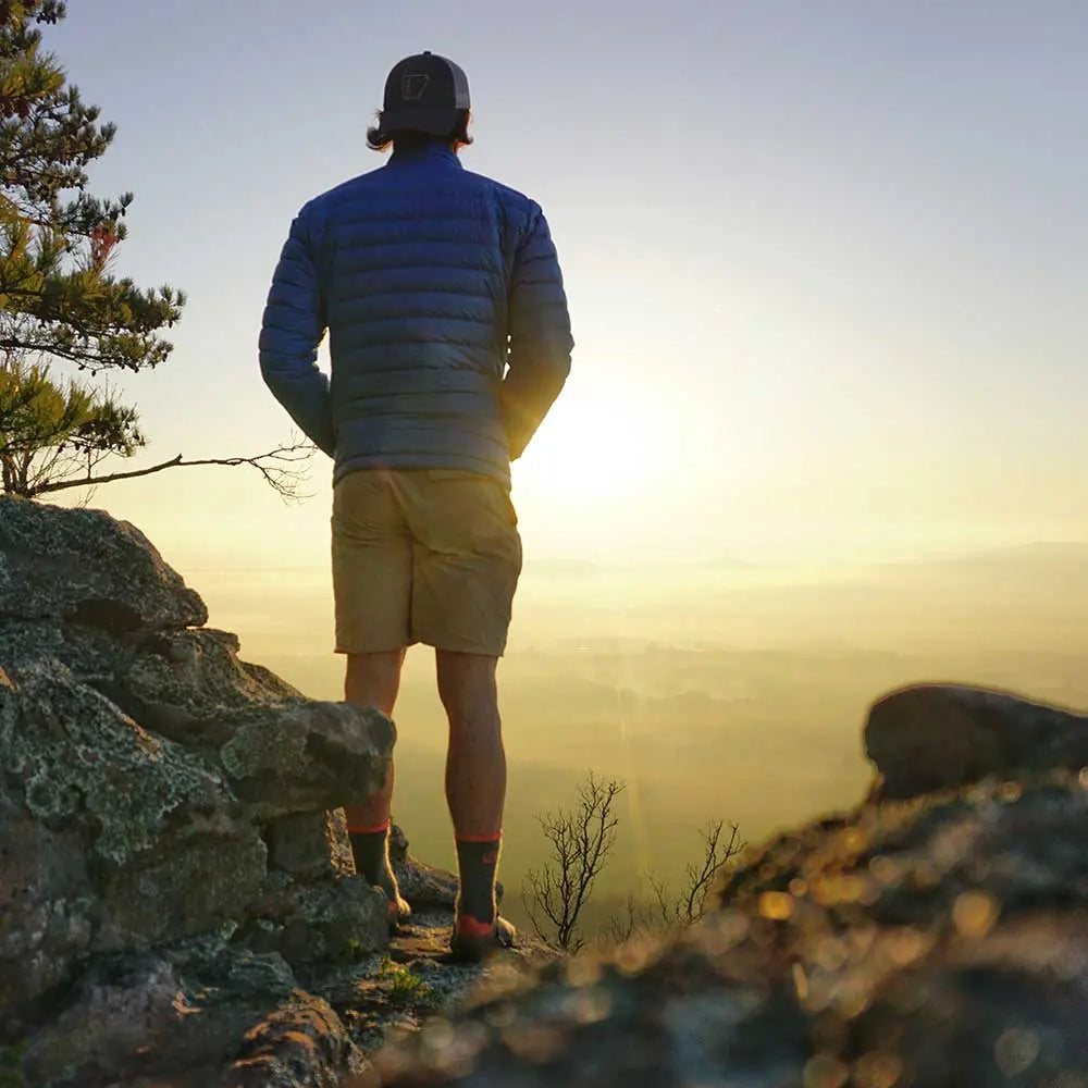 Man wearing Cloudline merino wool hiking socks watching sunset from mountain top.