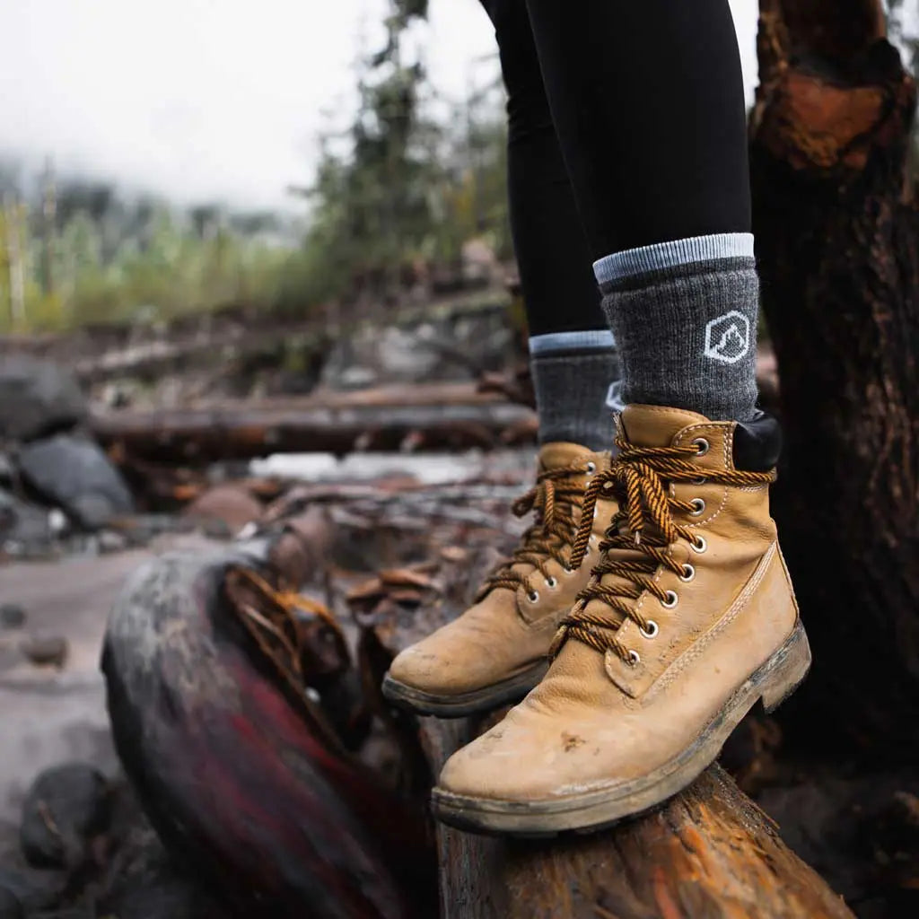 Women wearing Cloudline merino wool hiking socks standing on log over river.