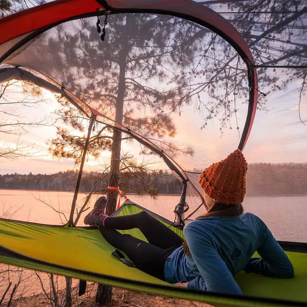 Women wearing Cloudline merino wool hiking socks laying in suspension tent by lake enjoying the sunset view.