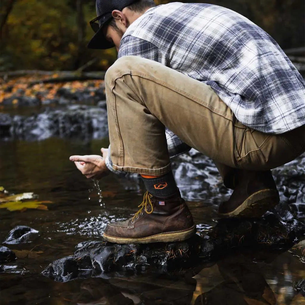 Man wearing Cloudline merino wool hiking socks crouching near water and scooping up water with hands.