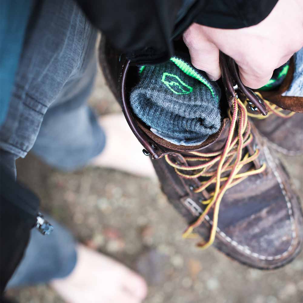 CloudLine ultralight merino wool hiking socks in a pair of boots held by barefoot hiker.