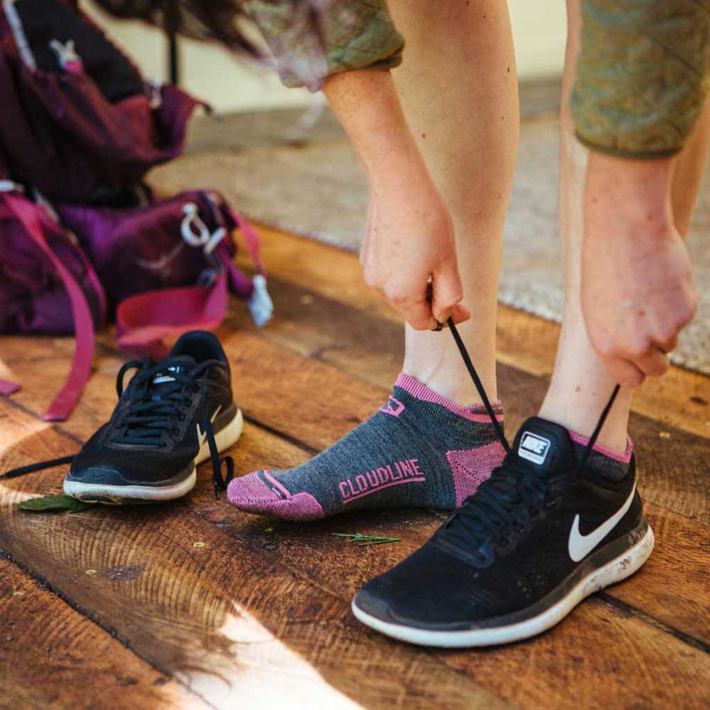 Women standing in cabin next to backpacking pack putting on Cloudline running socks and shoes. 