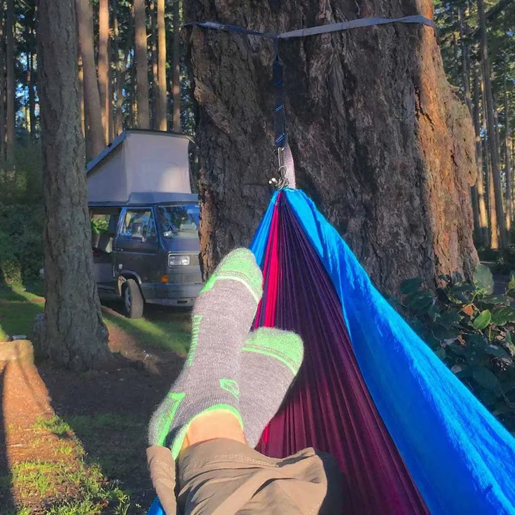 Camper wearing Cloudline merino wool running socks relaxing in hammock in front of vintage camper van.
