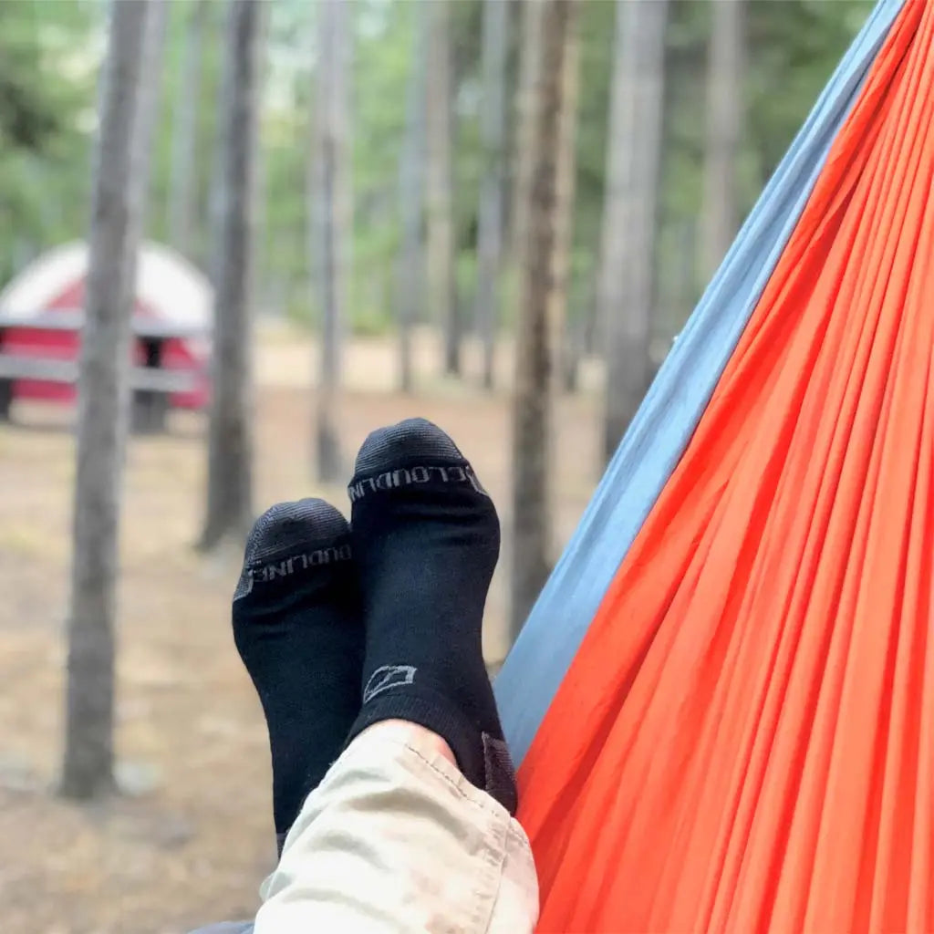 Camper wearing Cloudline no show merino wool socks laying in hammock near tent.