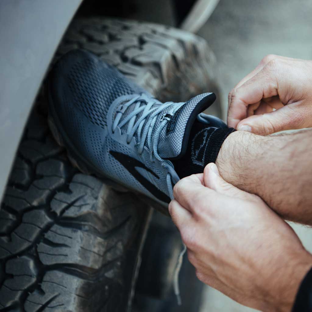 Man wearing Cloudline socks getting shoes tied with foot up on camper tire.
