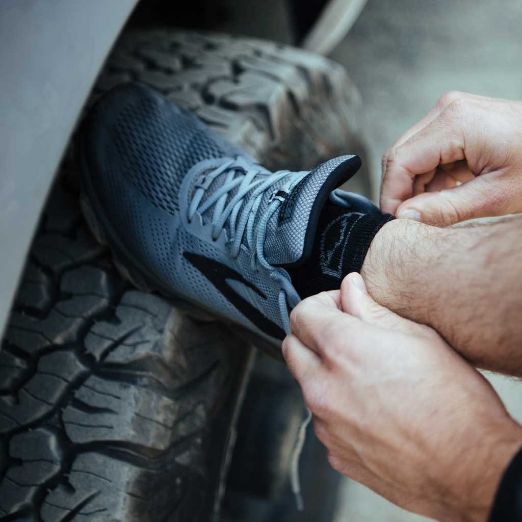 Man wearing Cloudline socks getting shoes tied with foot up on camper tire. 