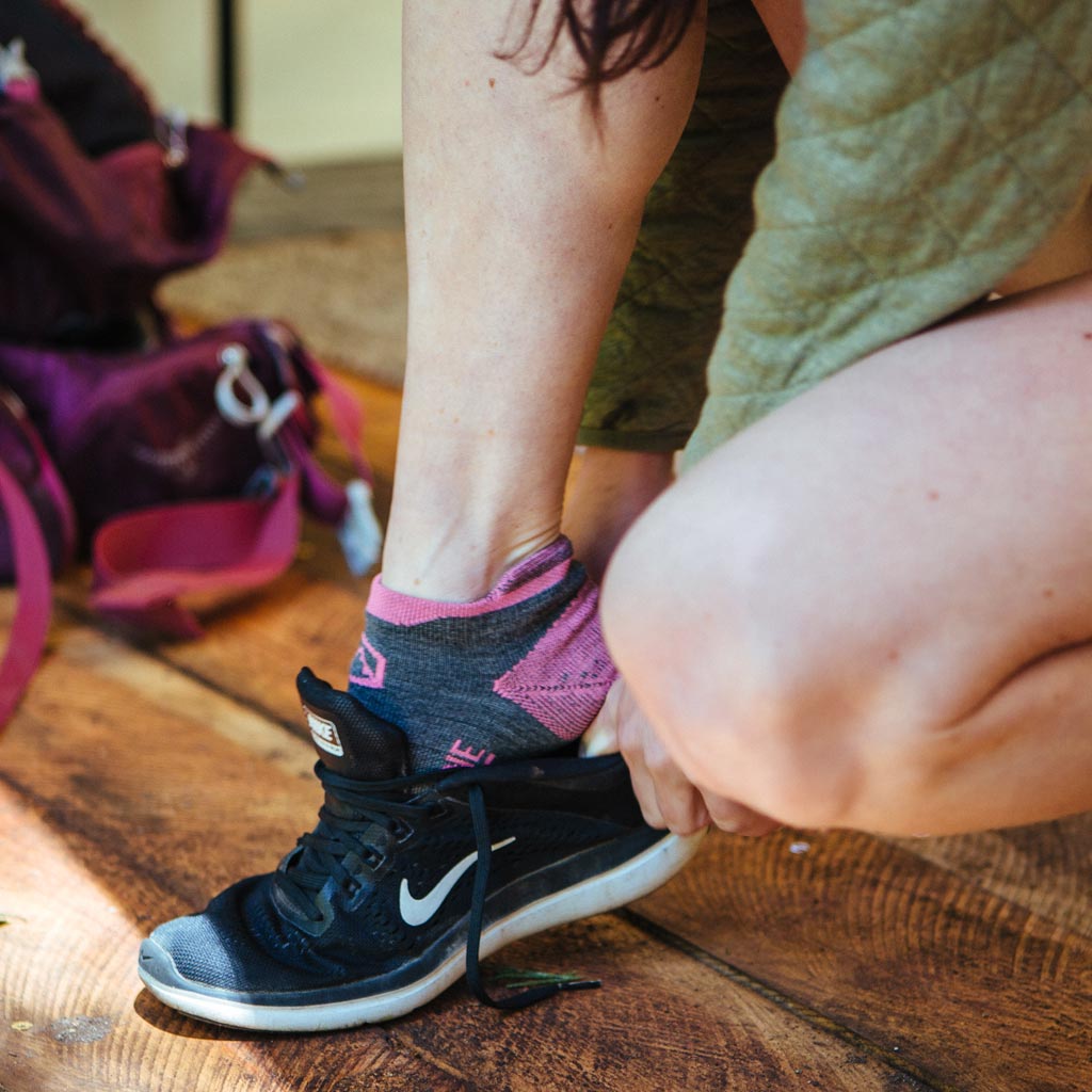 Runner wearing Cloudline socks crouching down to put on running shoe. 