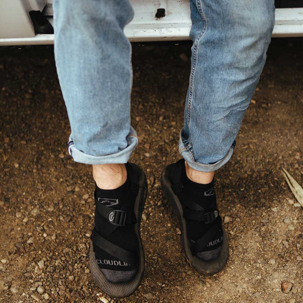 Man wearing Cloudline running socks and sandals sitting with feet out of camper van. 