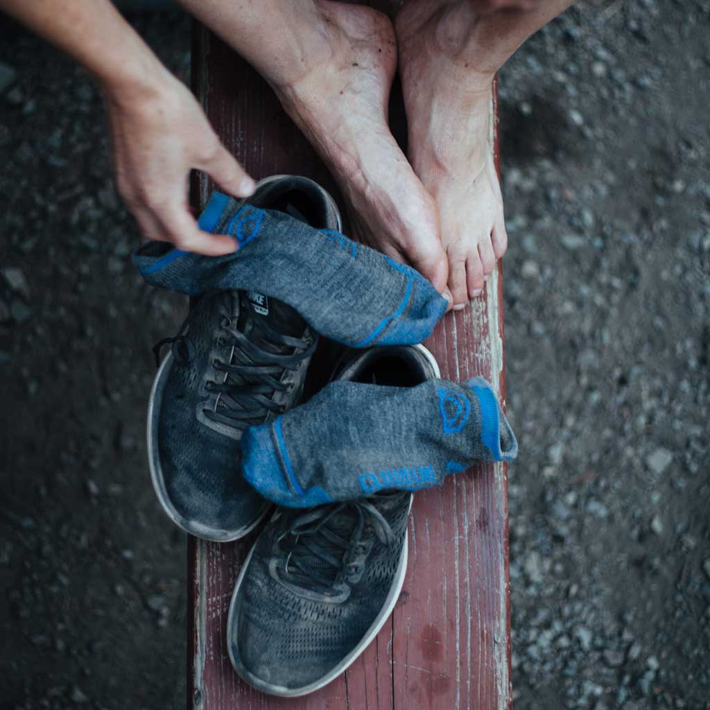 Runner sitting on red bench with Cloudline running socks and shoes sitting next to bare feet.