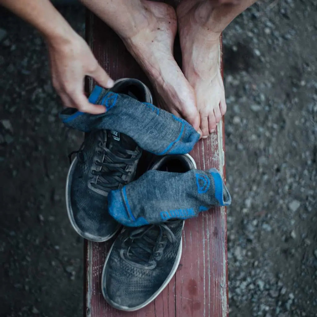 Runner sitting on red bench with Cloudline merino wool running socks and shoes sitting next to bare feet.