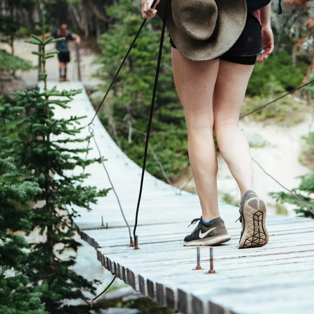 Women wearing Cloudline merino wool no-show socks crossing wooden suspension bridge.