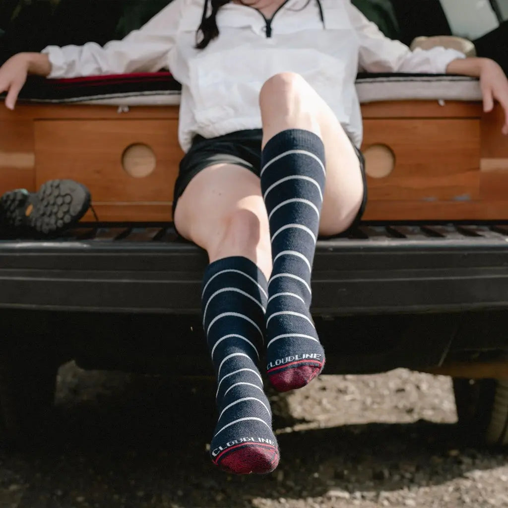 Women wearing Cloudline merino wool compression socks sitting on the back of camper truck sticking feet out.