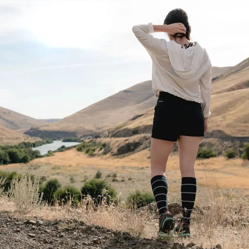 Women wearing Cloudline merino wool compression socks with back to camera looking at river and mountain view.