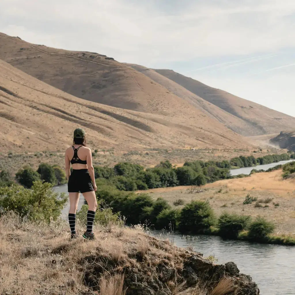 Trail runner wearing Cloudline merino wool compression socks pausing to enjoy the view of mountains and river valley.