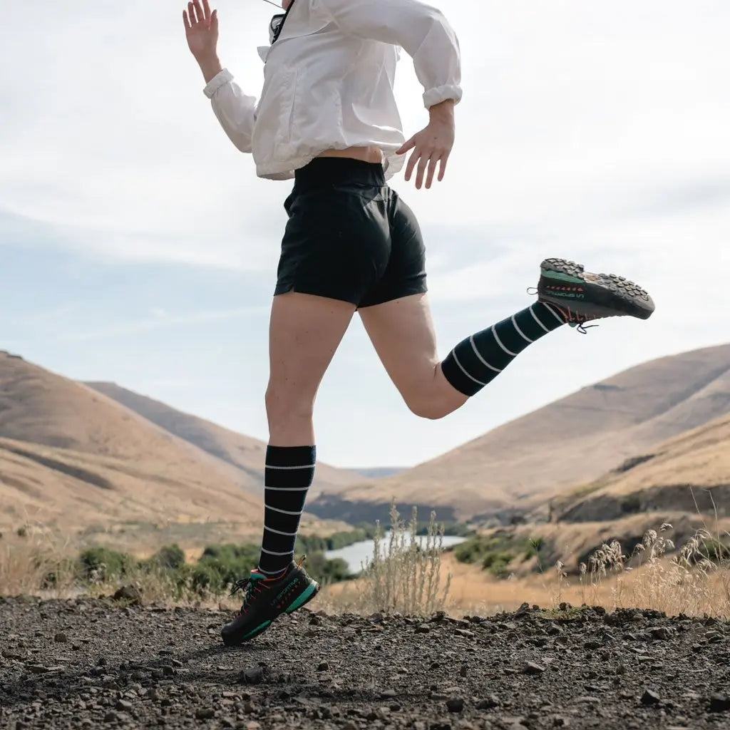 Women mid stride while trail running wearing Cloudline merino wool compression socks.