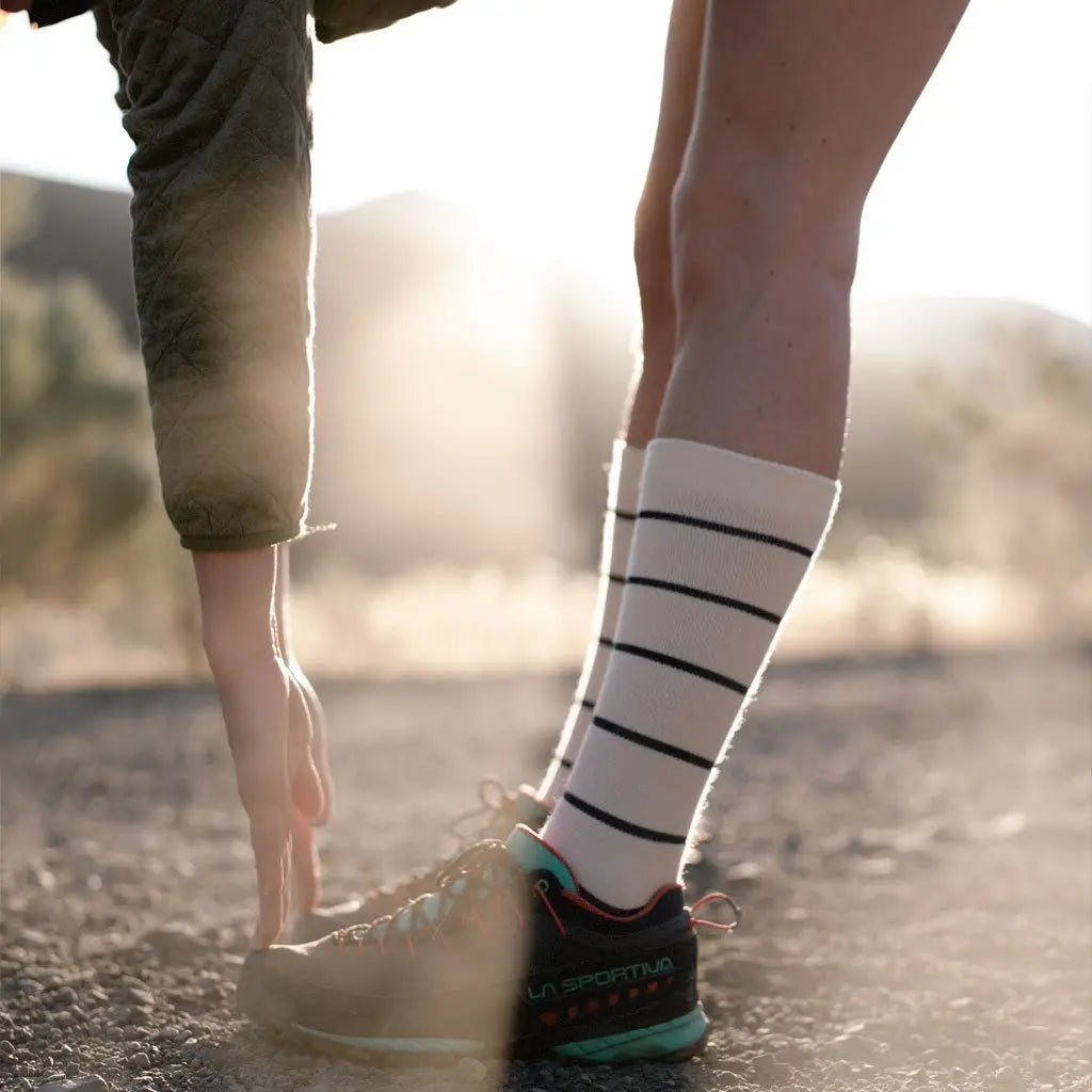 Runner wearing Cloudline merino wool compression socks stretching to touch toes before morning run.