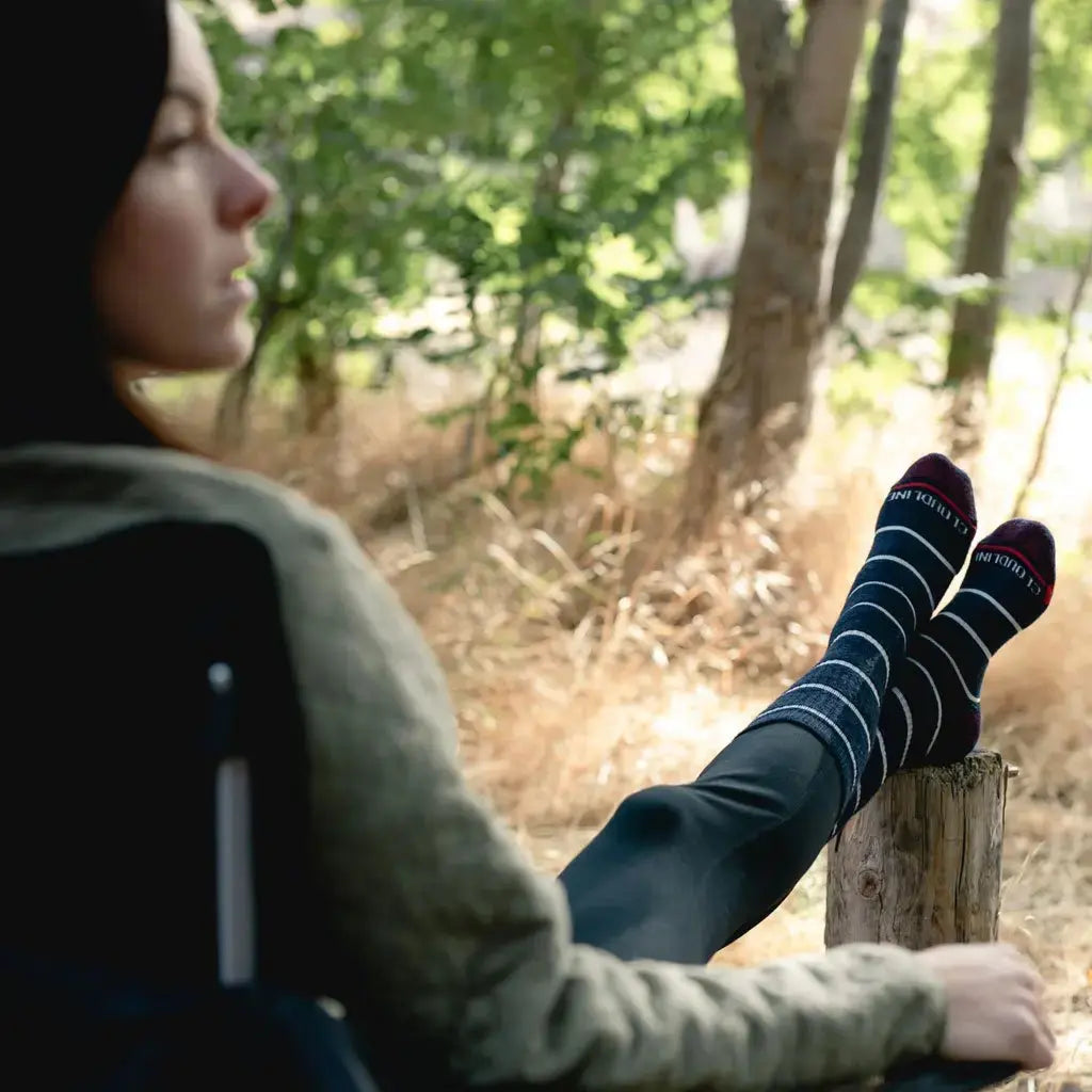 Women wearing Cloudline merino wool hiking socks sitting in camp chair with feet up on log.