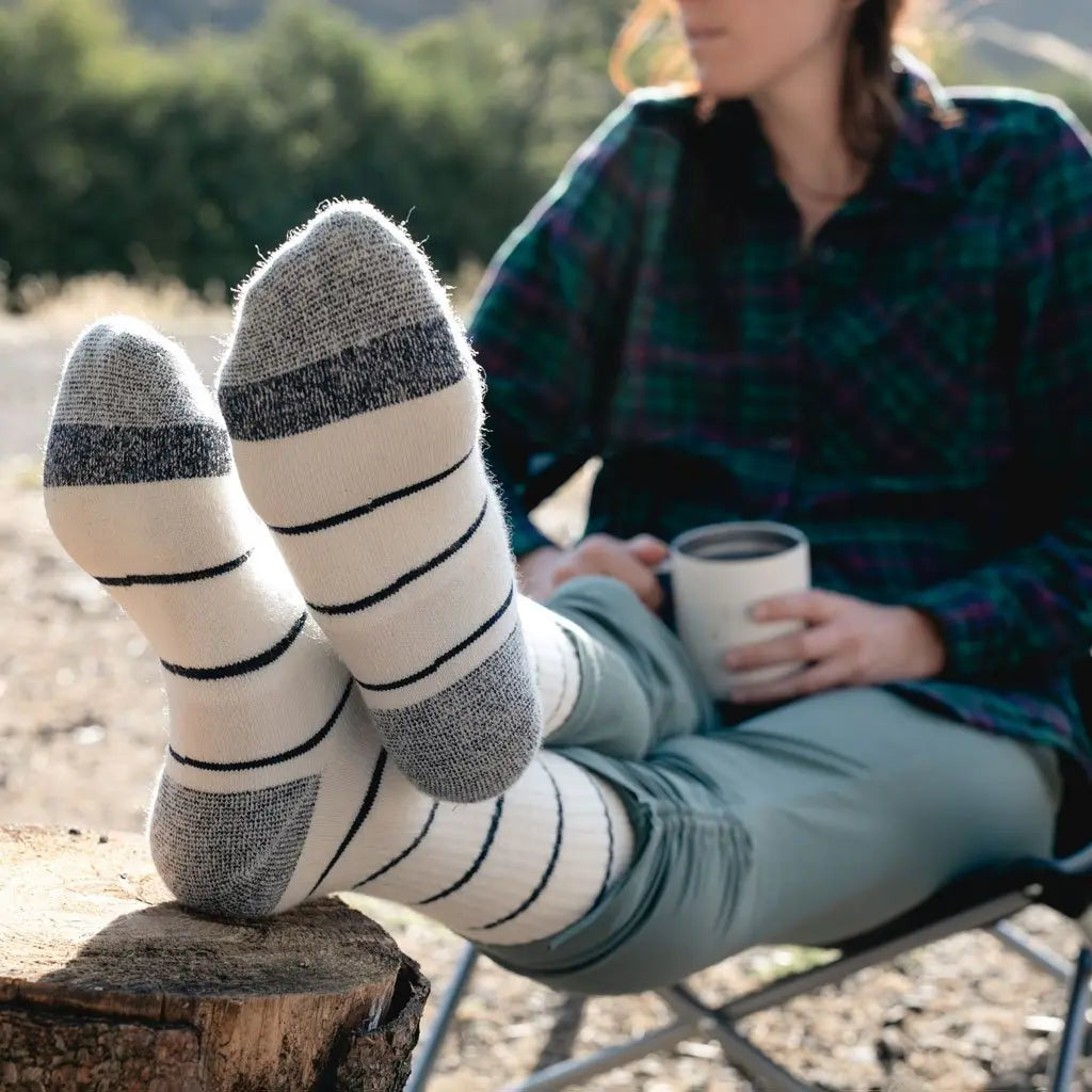 Women wearing Cloudline merino wool hiking socks, sitting in camp chair drinking coffee.