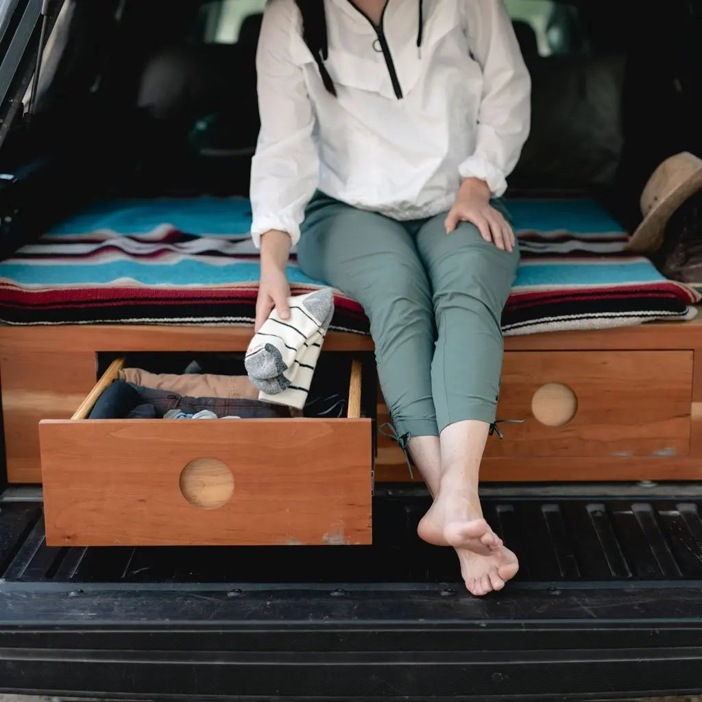 Women sitting on camper truck bed putting neatly folded Cloudline merino wool hiking socks into drawer.