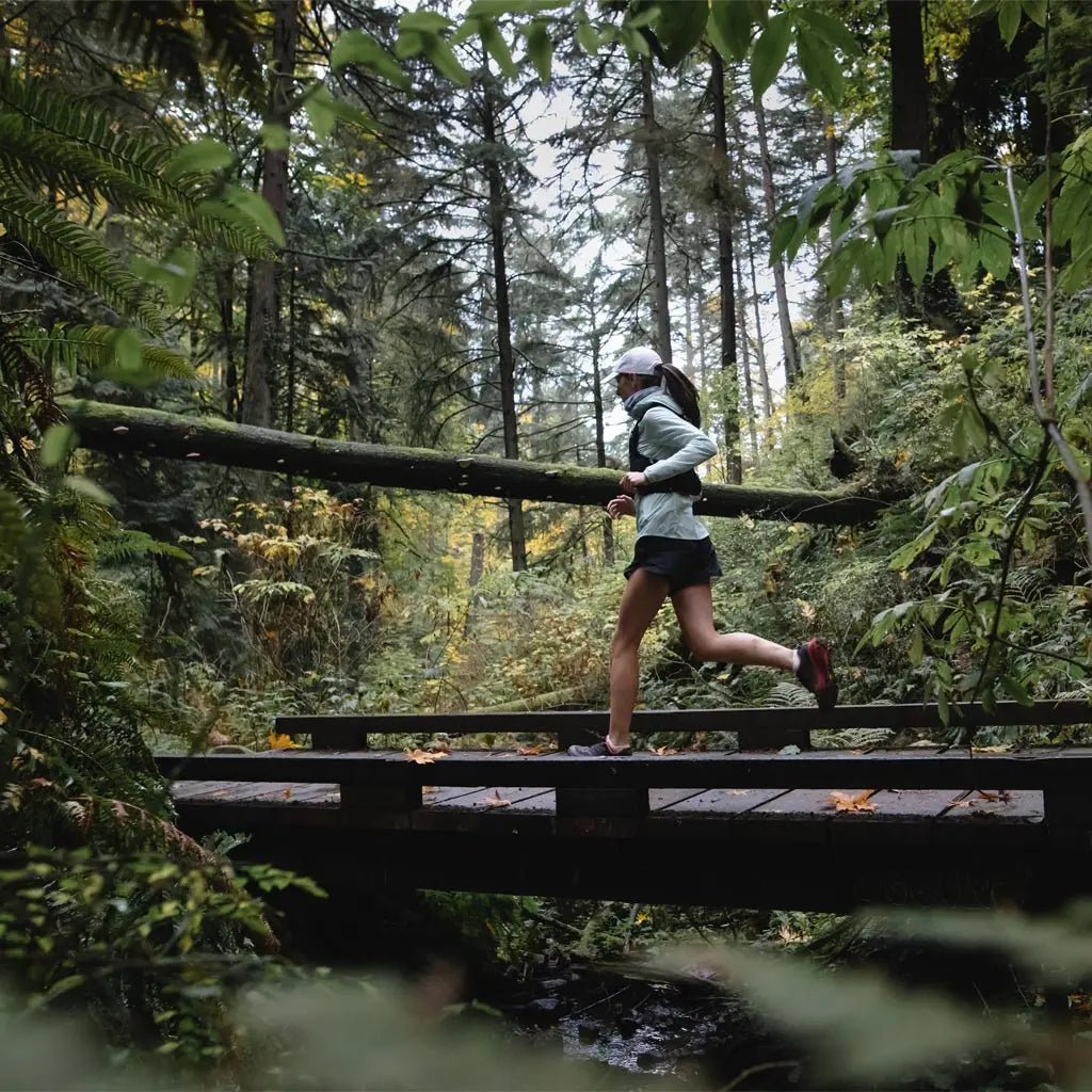 Trail runner wearing Cloudling merino wool no show socks while running across wooden bridge.