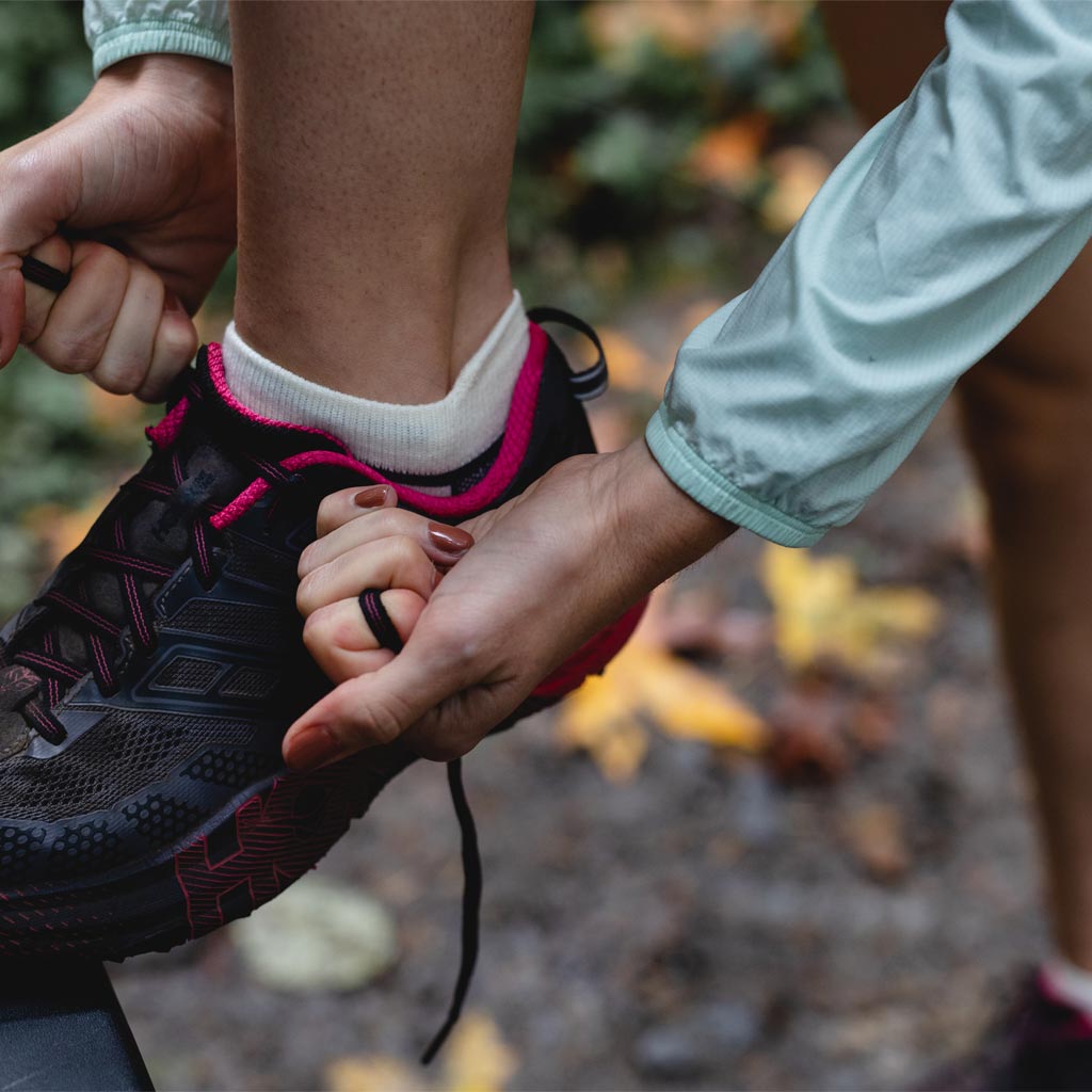 Close up of runner wearing Cloudline socks tying shoe before run. 