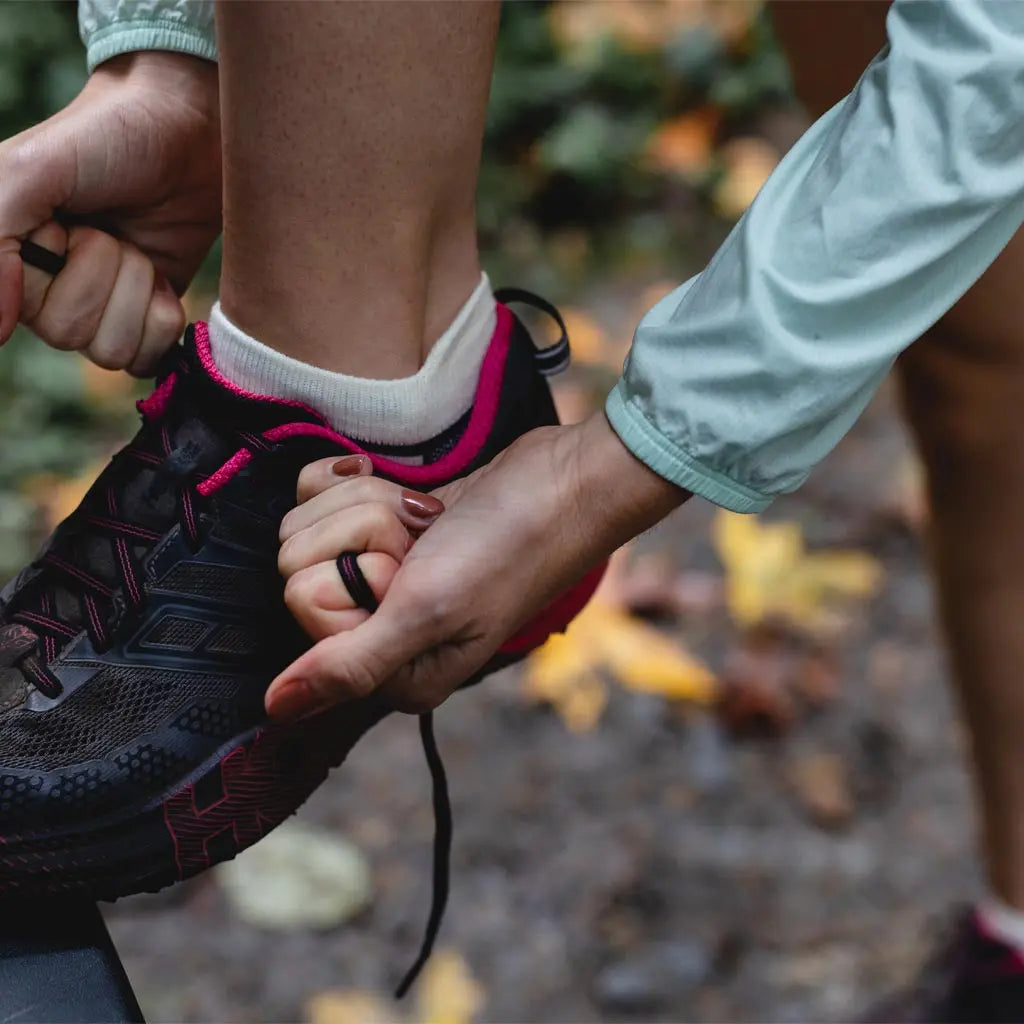 Close up of runner wearing Cloudline merino wool trail running socks tying shoe before run.