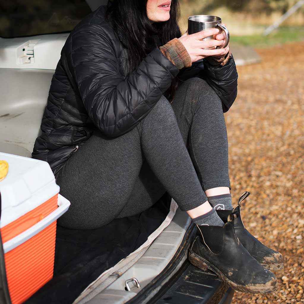 Camper sitting on back bumper having coffee wearing Cloudline merino wool socks.