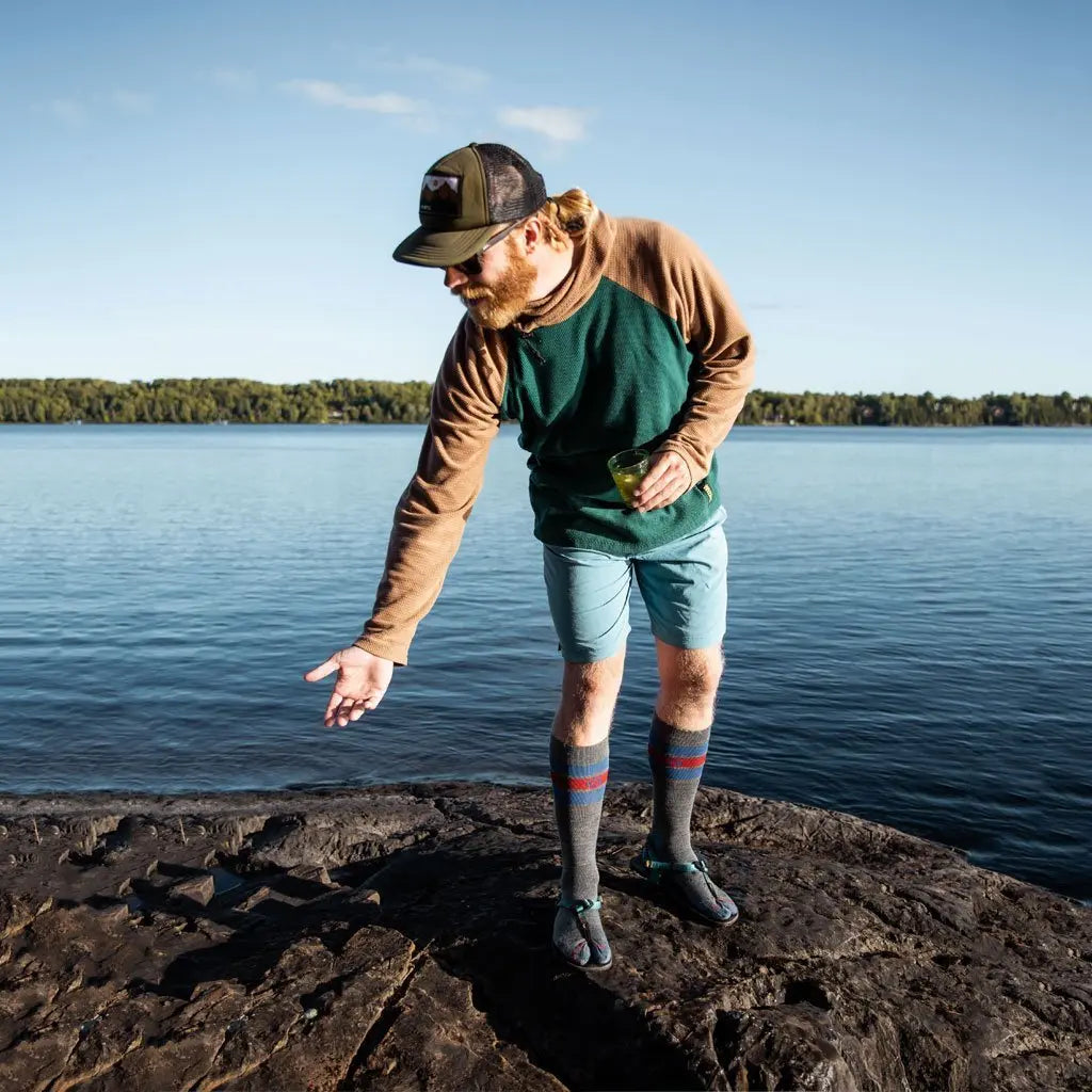 Man wearing Cloudline merino wool compression socks and sandals standing on lake edge.