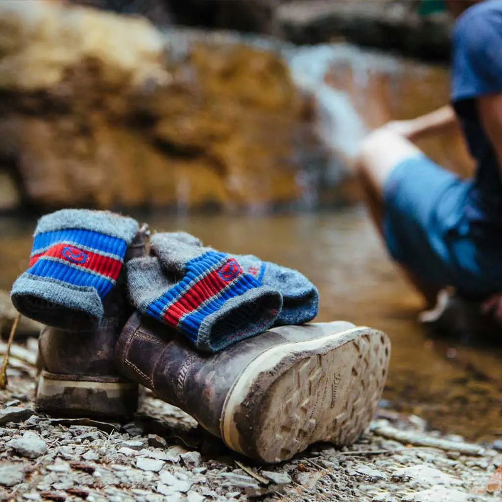 Cloudline merino wool hiking socks on top of leather boots while hiker sits with feet in water in front of water fall.