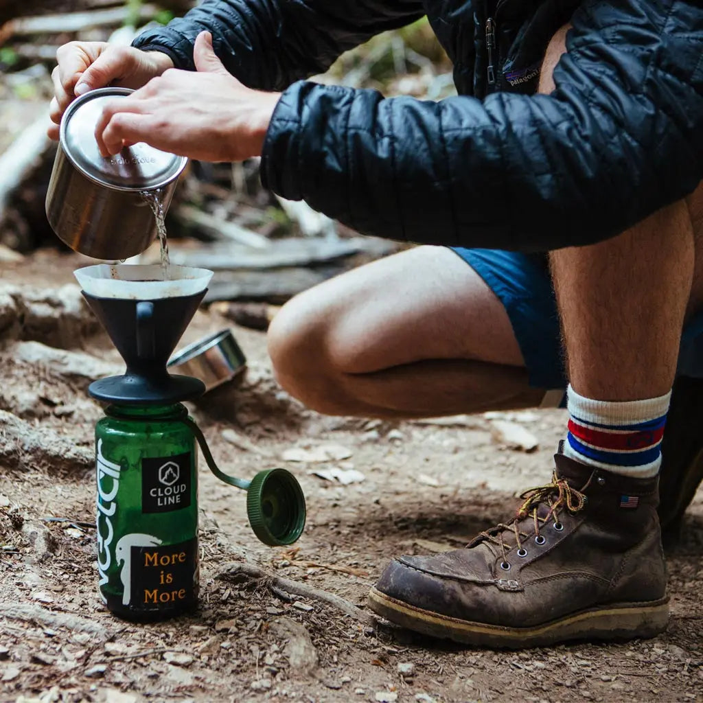 Backpacker wearing Cloudline merino wool hiking socks crouched down to make pour over coffee.