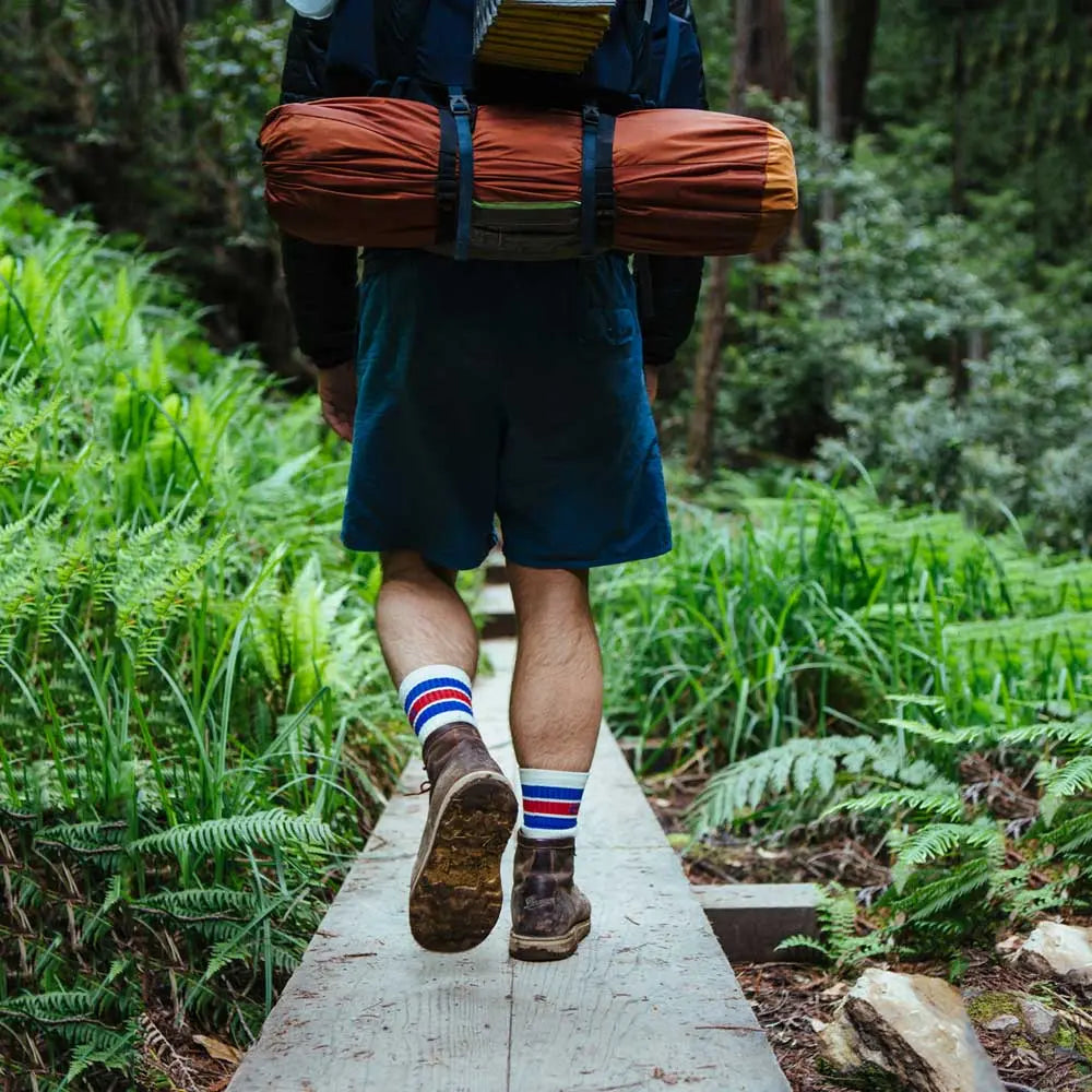 Backpacker wearing Cloudline merino wool hiking socks walking away from camera on forest trail.