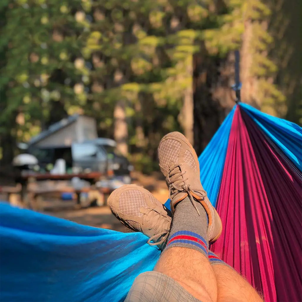 Camper wearing Cloudline merino wool hiking socks laying in hammock with camper van in background.