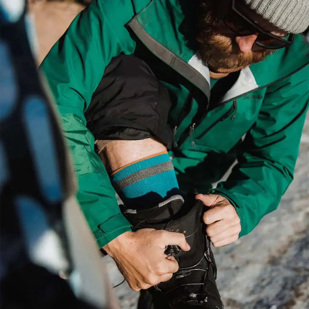 Snowboarder wearing Cloudline merino wool snow socks with foot up on bumper to fasten boots.