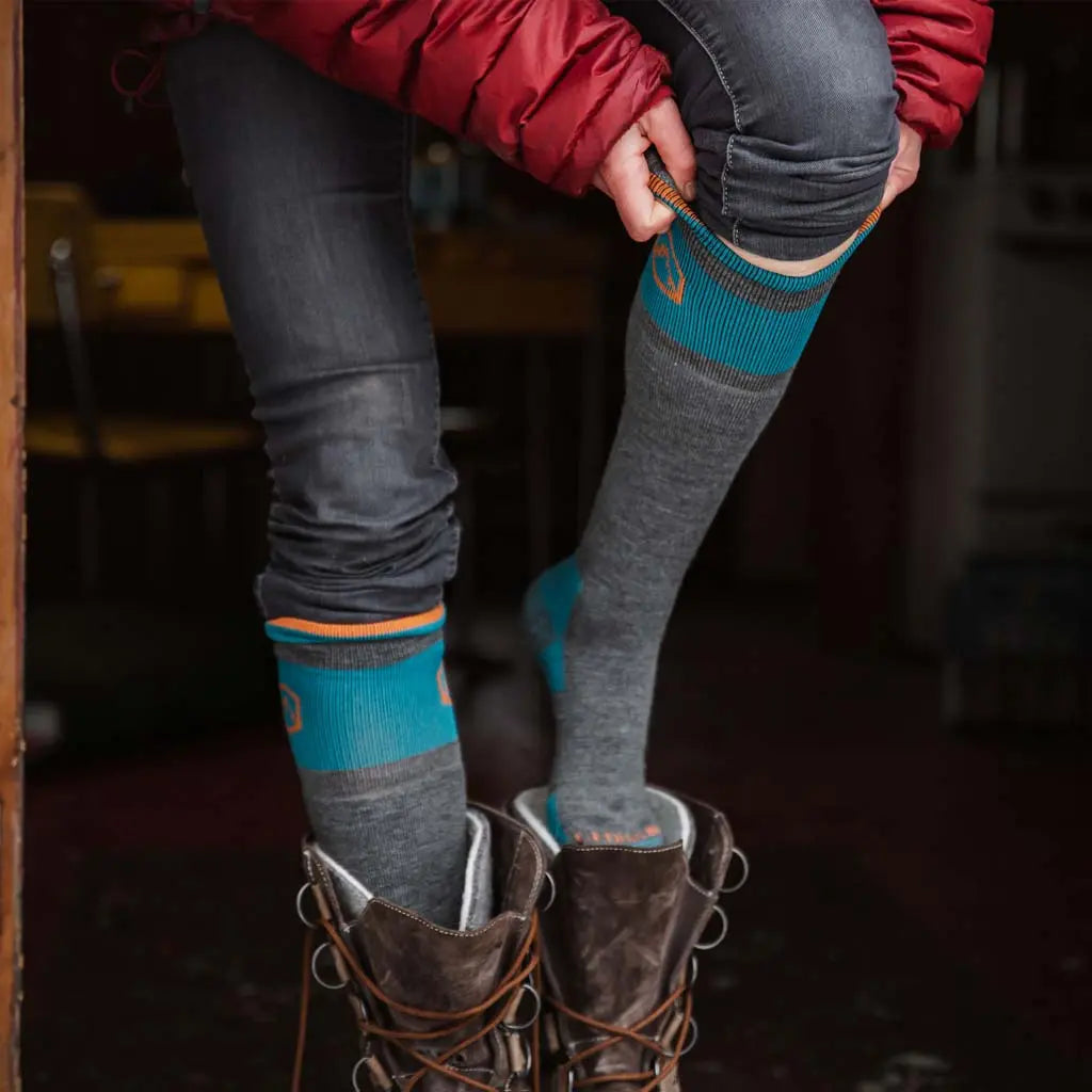 Women standing in cabin putting on Cloudline merino wool snow socks and winter boots.