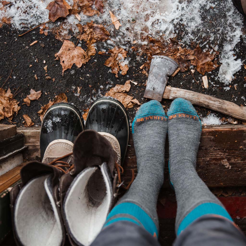 Women wearing Cloudline socks standing in snowy cabin doorway with boots next to her.