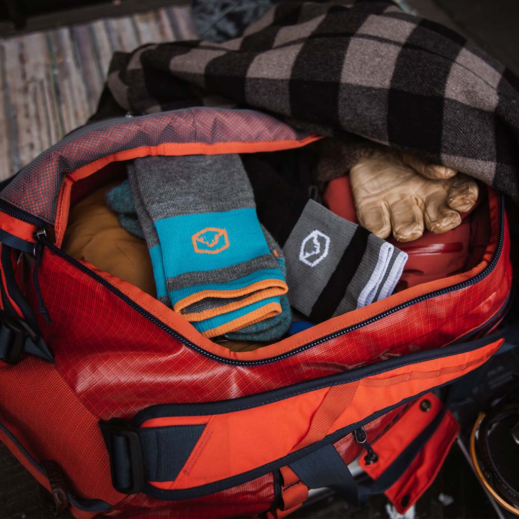 Duffle bag full of snow gear with Cloudline ski and snowboard socks sitting on the top.